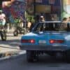 Vintage blue car parked on city street with mural art in background.