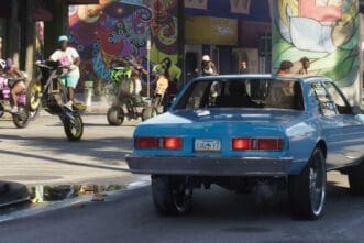 Vintage blue car parked on city street with mural art in background.